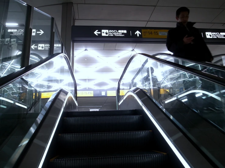 a man standing at an escalator in a terminal, near a light display
