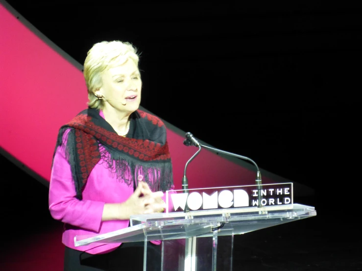 a woman giving a speech with a red and pink background