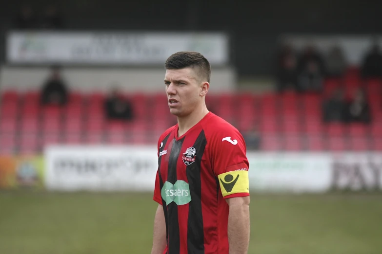 the young man in the red and black soccer shirt stands on the field