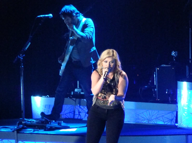 a lady singing into a microphone while standing next to an older man on stage