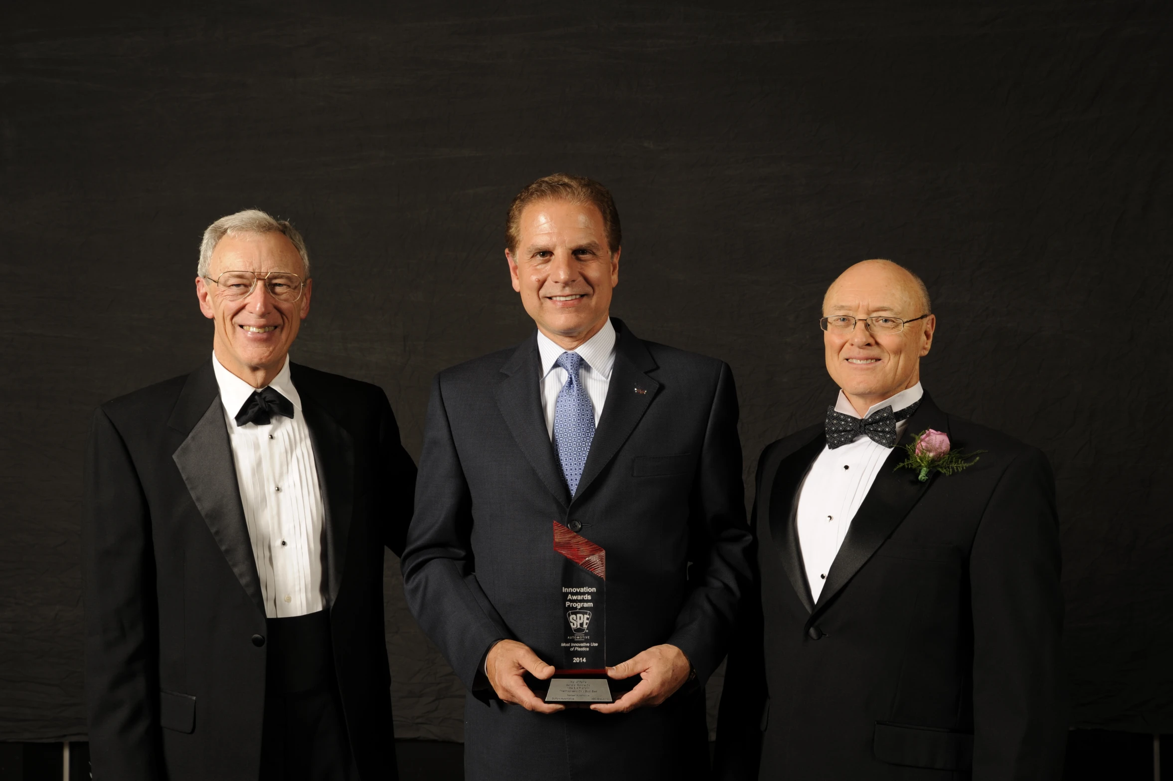 three men are holding an award in a formal setting