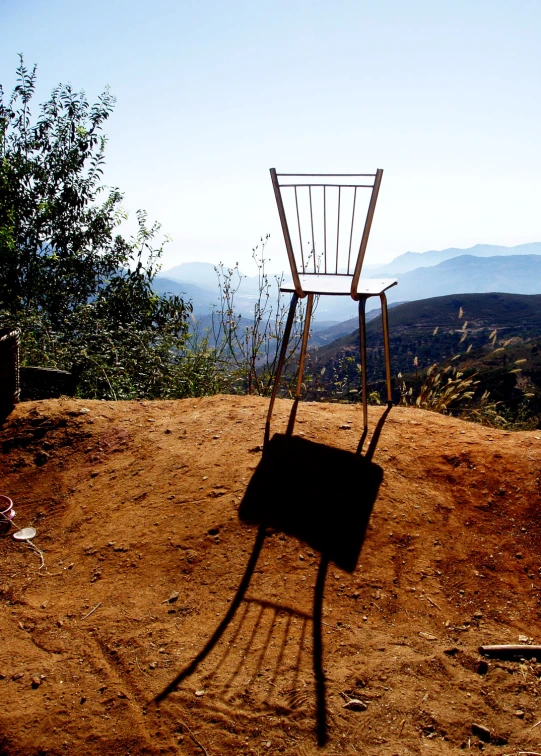 a lone chair sits on the dirt on a hill