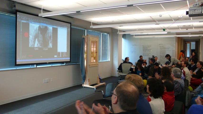 a group of people standing around a room with a projector screen