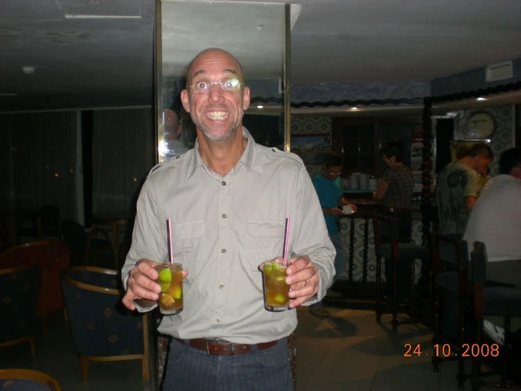 a man in a tan shirt holding two glasses with drink