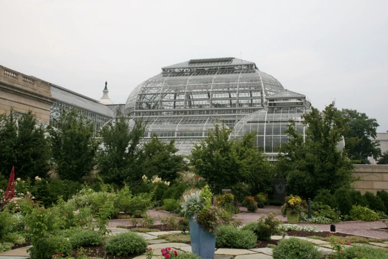 a large green house with glass walls and lots of flowers and trees around it