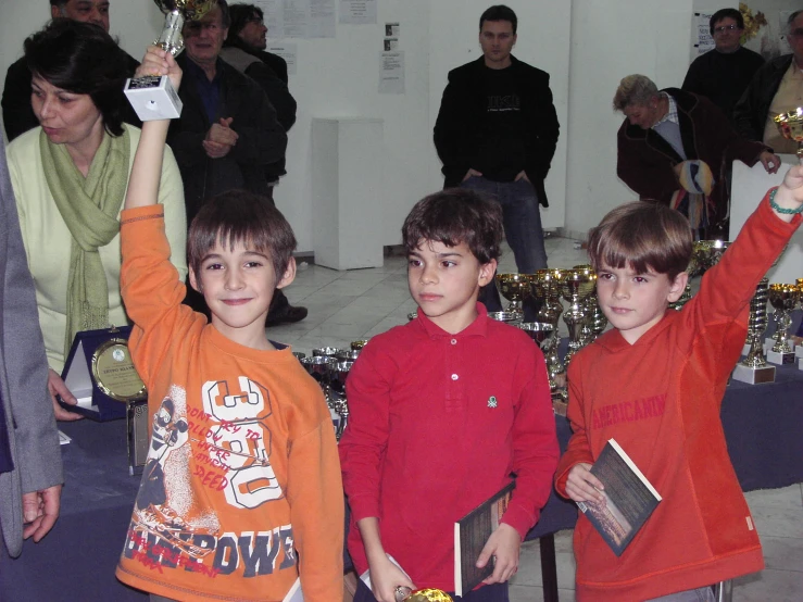 three boys holding up trophies in front of people