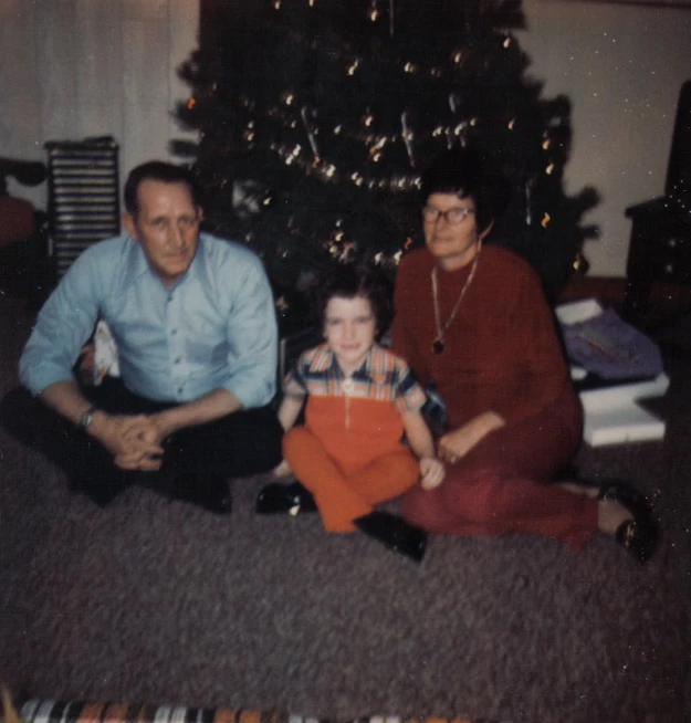 an older man and two women sit on the floor next to a small boy with his hand on his hip