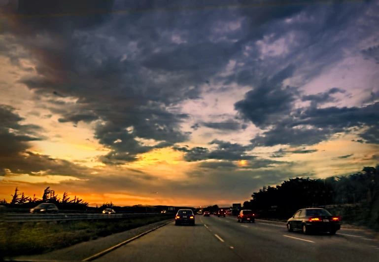 a bunch of cars traveling down the highway at sunset