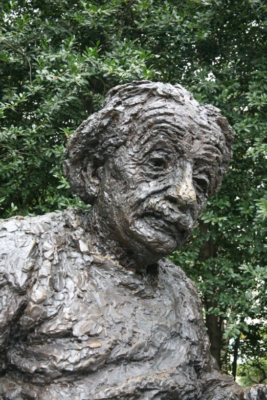 a large statue of an older person is sitting under a tree