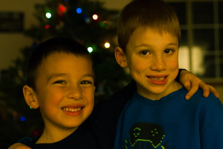 two boys posing in front of a christmas tree