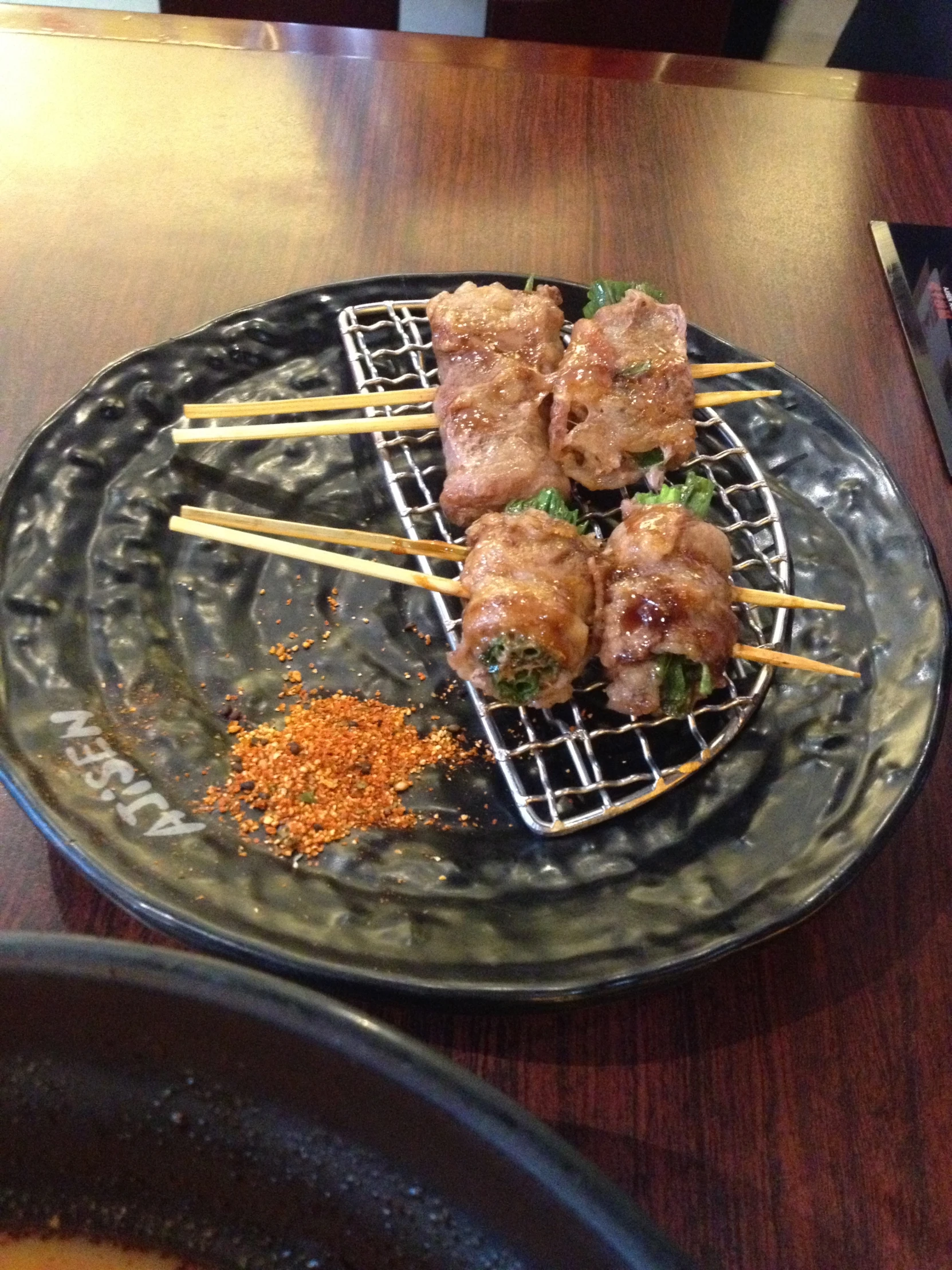 several skewers of food sit on a black plate