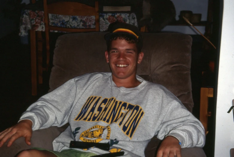 smiling boy wearing university shirt and cap sitting in a chair