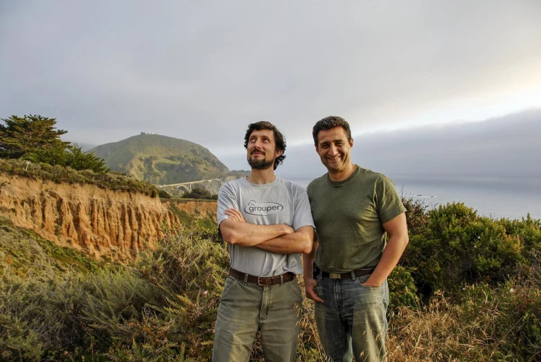 two men pose together on a hill, looking into the camera