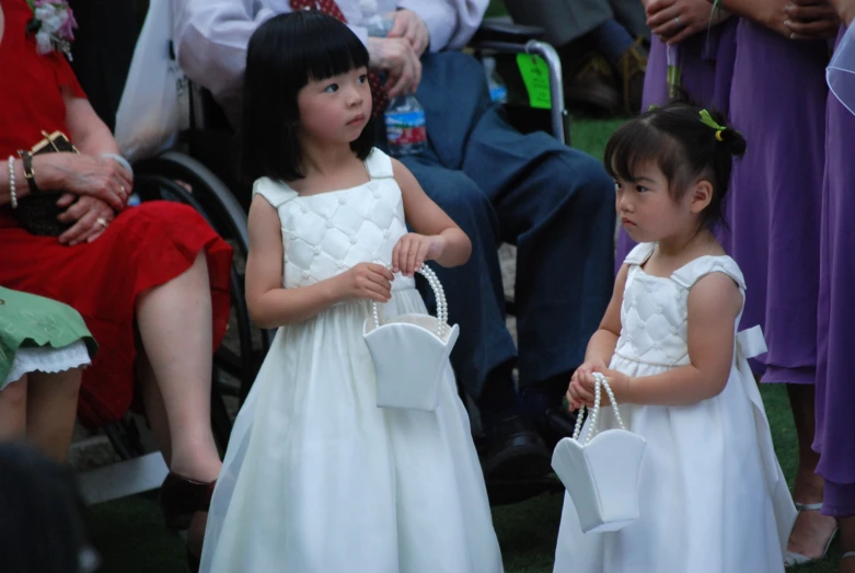 two little girls in white dresses carry purses in each other's hands