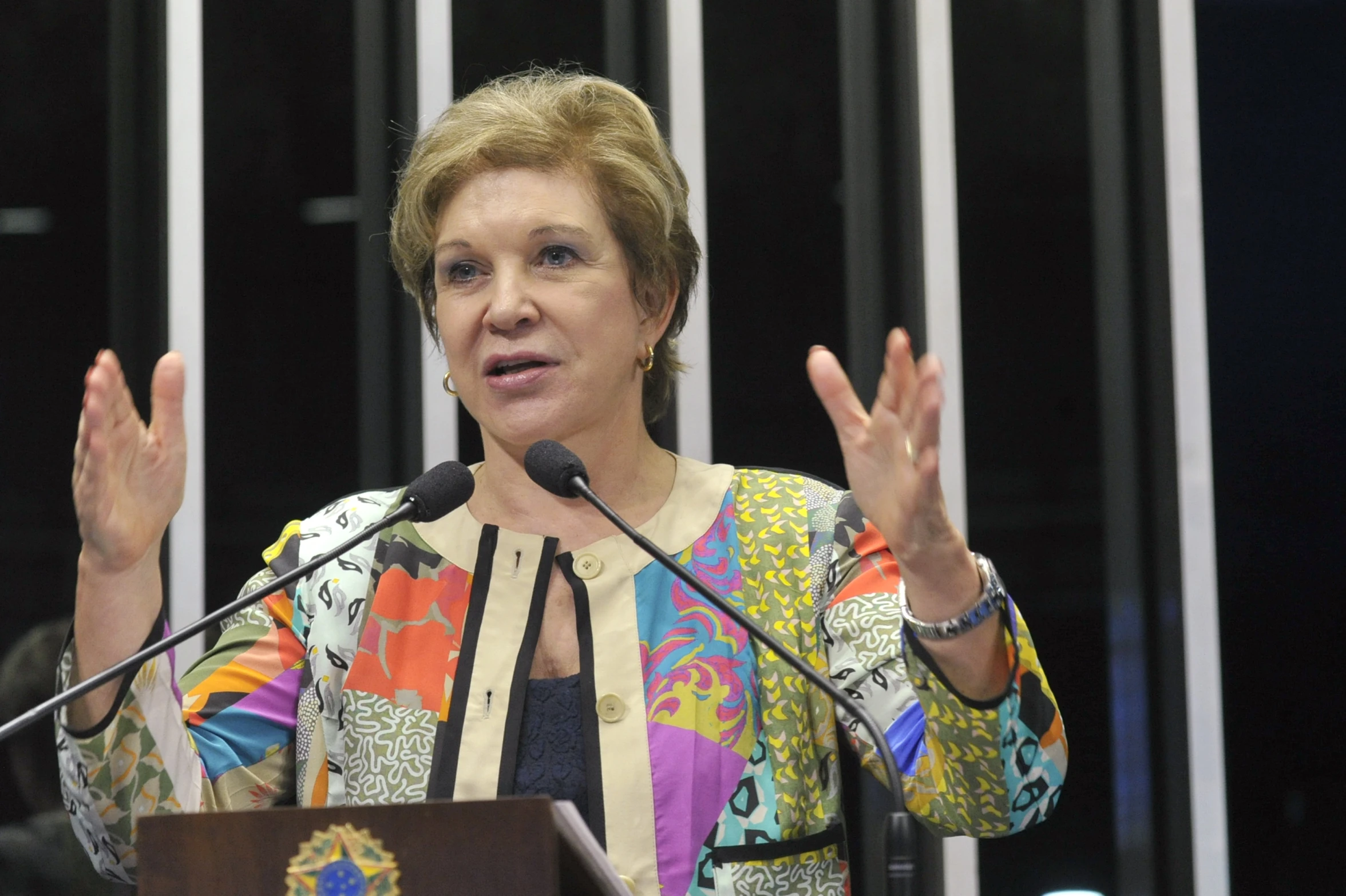 a woman is standing at a podium holding her hands up