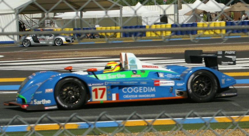 a race car in motion on the track behind a fence