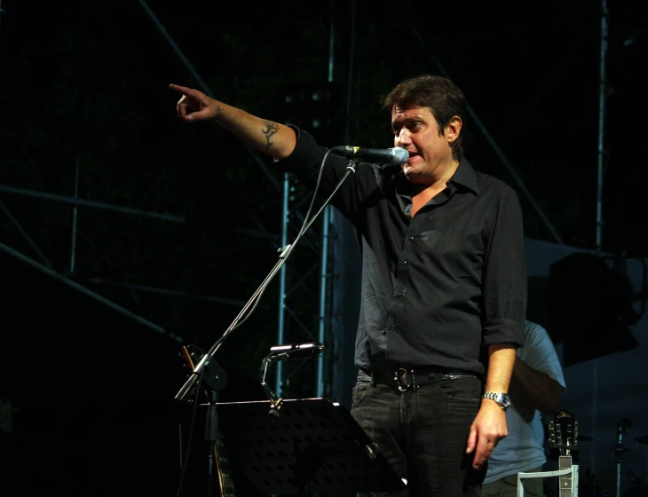 a man holds a guitar and points with his hand in front of a microphone