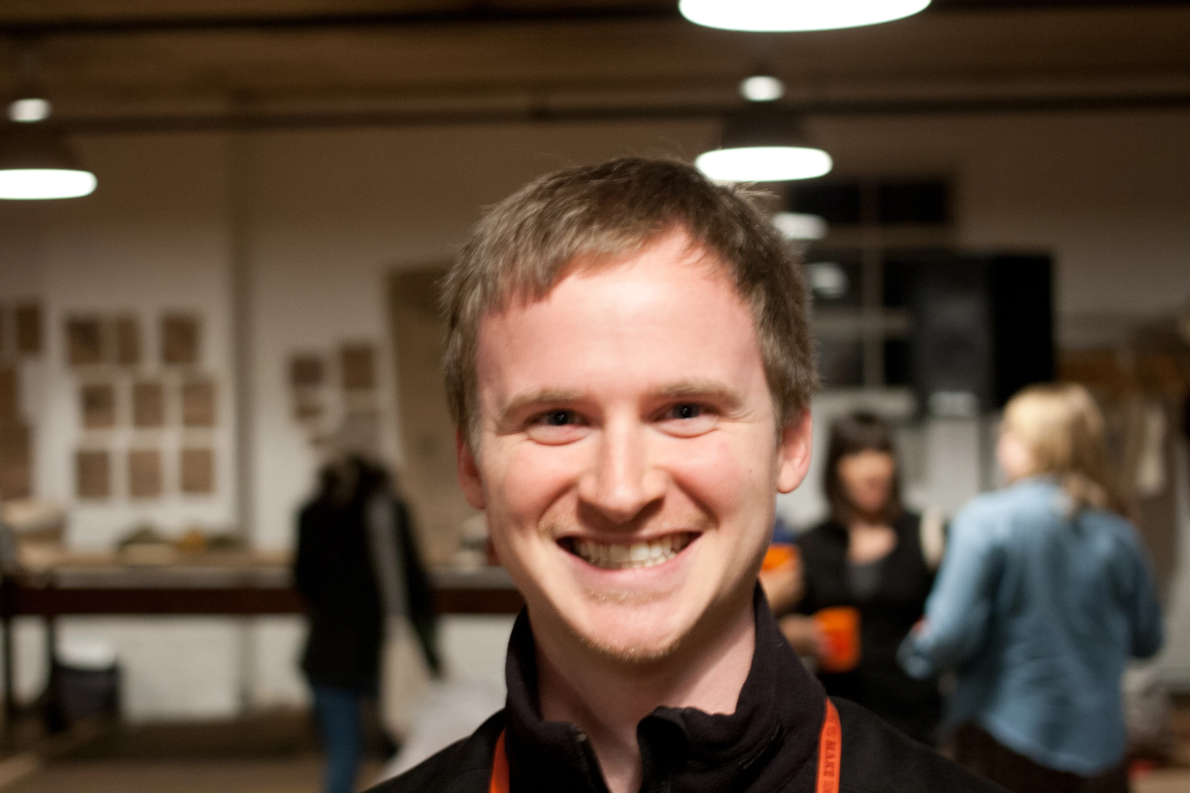 smiling man with an orange tie standing in front of people