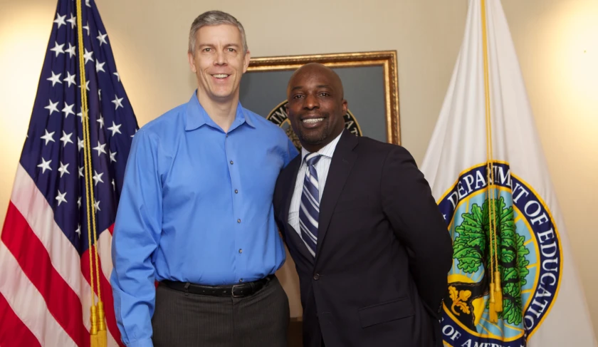 a man poses for a picture with another man in front of a flag