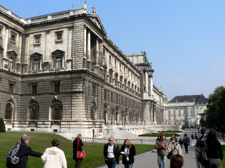 people walking along a walkway in front of a large, historic building