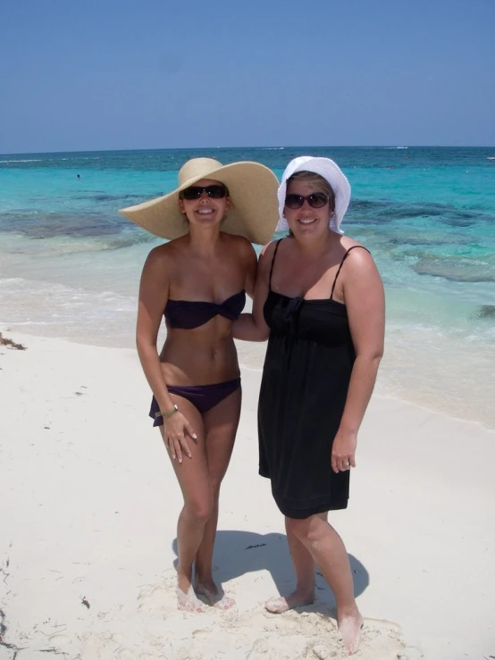 two woman standing on the beach while wearing hats