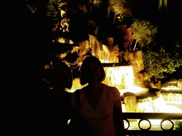 a couple standing in front of a waterfall at night