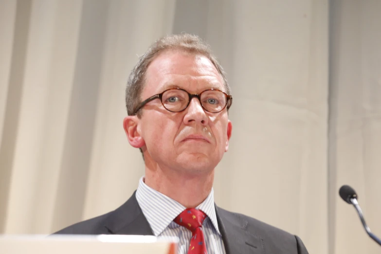 man with glasses sitting in front of a podium