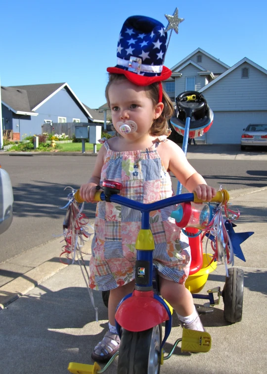 a  rides on her tricycle and wears a patriotic top hat