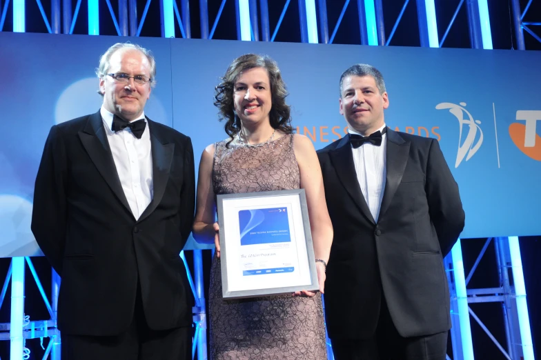 three men and a woman posing in front of a backdrop with an award on their lap