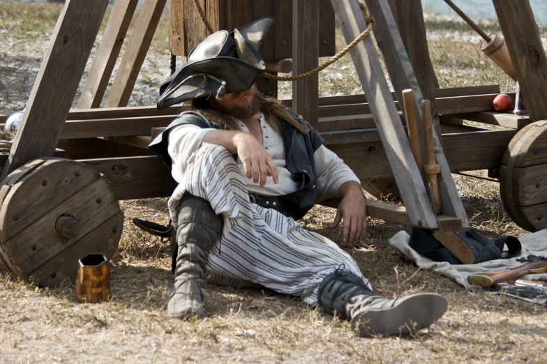 a man sitting on the ground next to a wooden structure