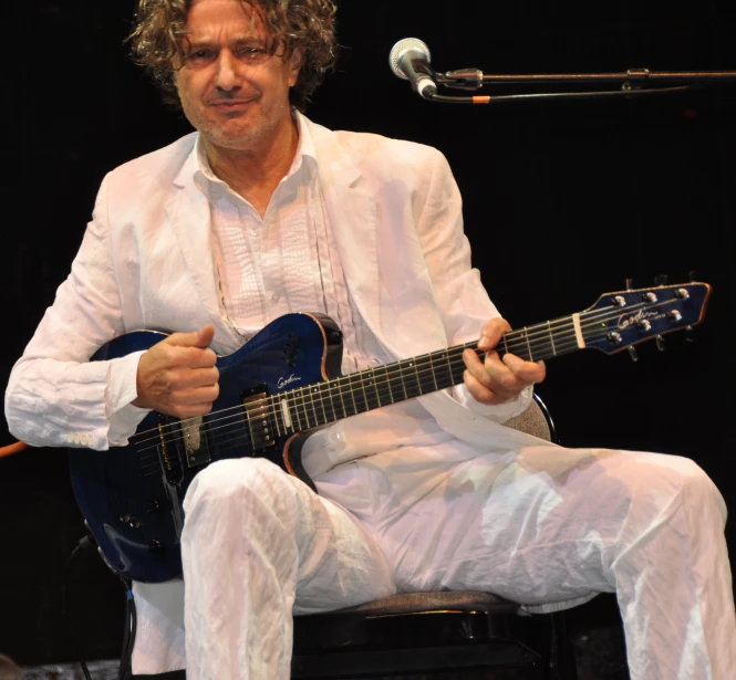 a man sitting with a guitar in front of a microphone