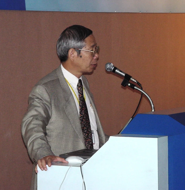 an older man stands at a podium speaking into a microphone