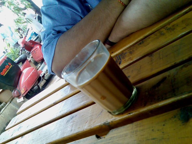 a person sitting at a wooden bench holding a glass