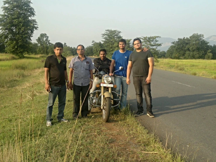 five guys and their motor bike are standing beside the road