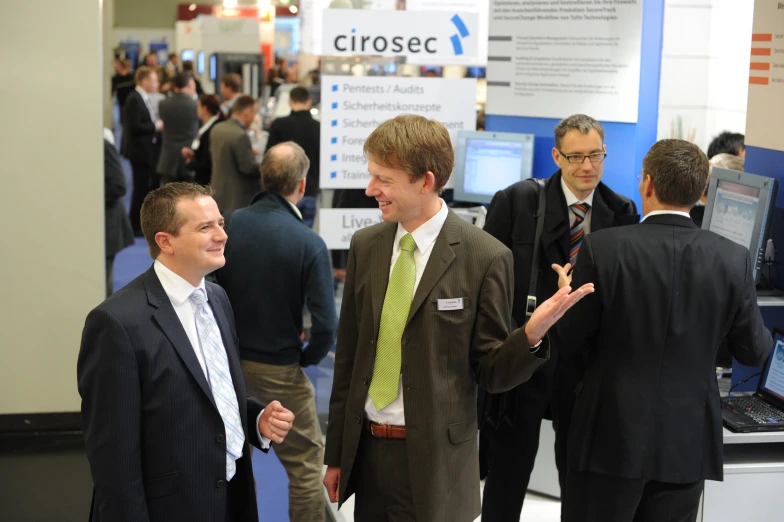 two men talking at an exhibit with the background displaying an advertit