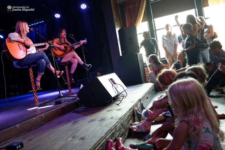 two women playing guitars on stage in front of audience