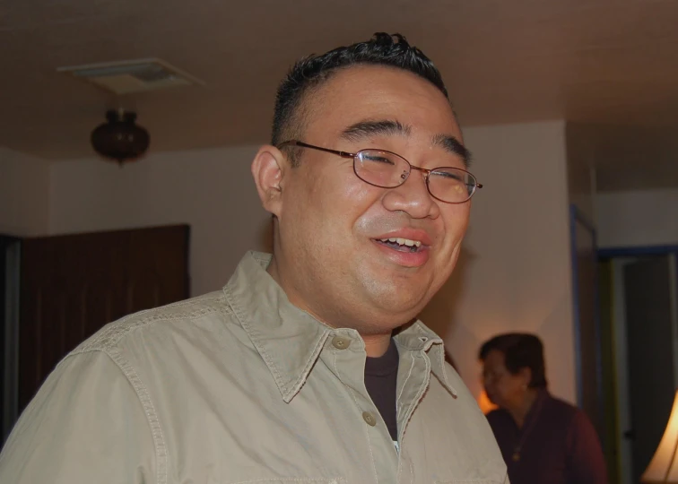 a man in glasses smiles while standing in a living room