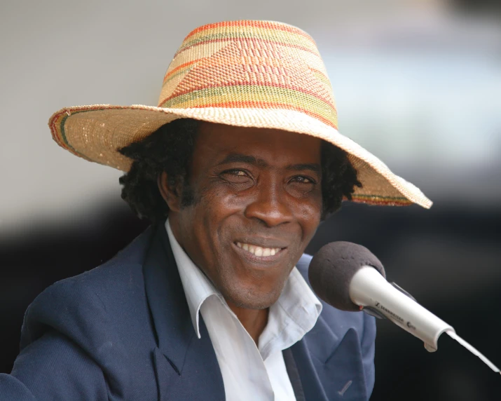 a smiling man wearing a straw hat next to a microphone