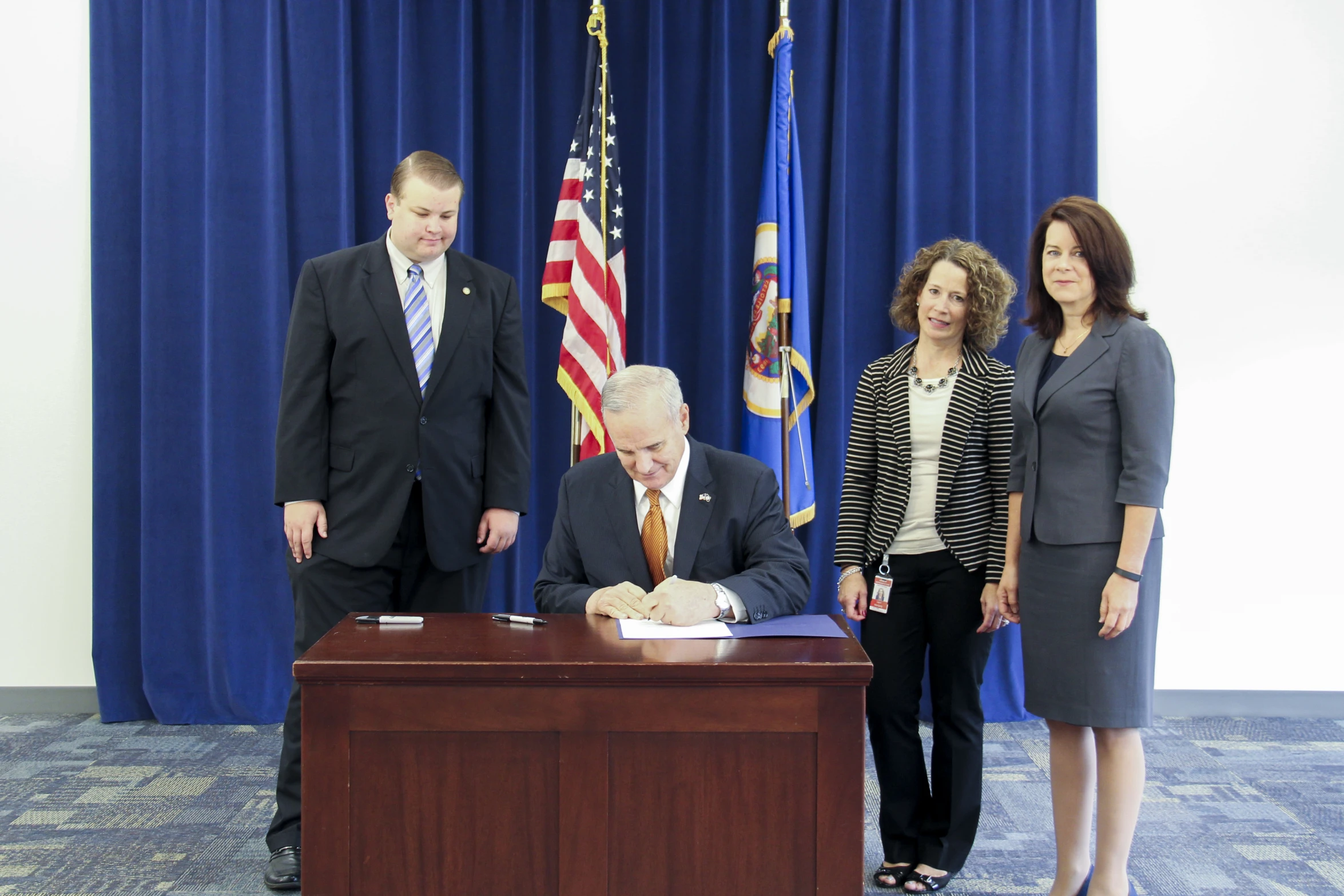 three people and two woman stand behind the official table signing the letter