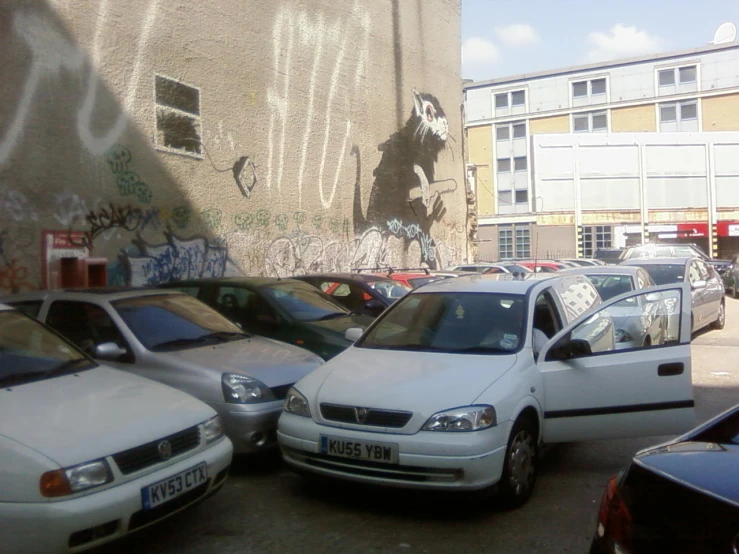 several vehicles parked by one another and some graffiti on the wall
