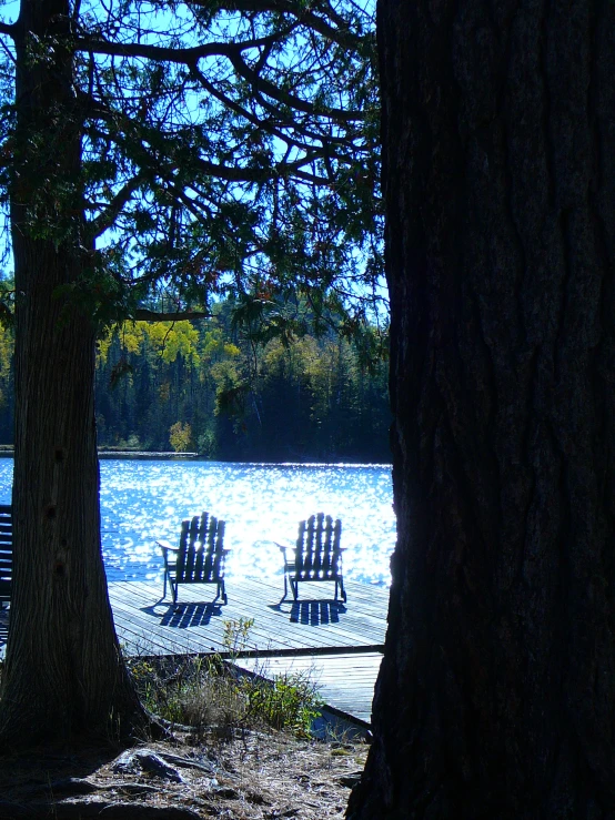 two empty adirondack chairs set up in front of a lake