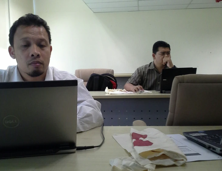two men sitting at desk in front of laptops