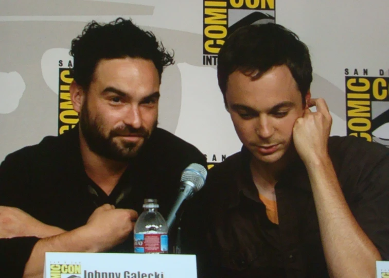 a man in black shirt sitting next to another person at microphone