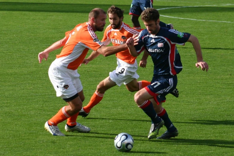 two soccer players in orange and white battle for the ball