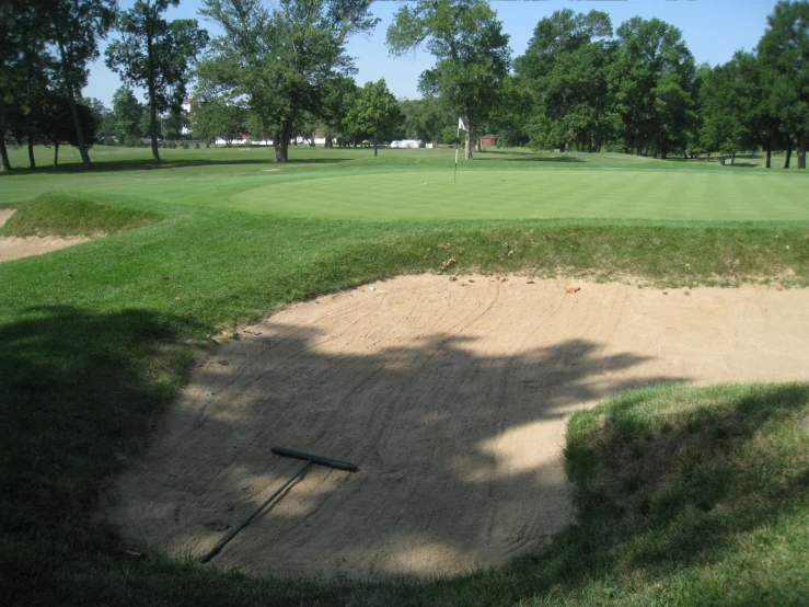 an empty dirt course on the green in the distance is an artificial golf hole