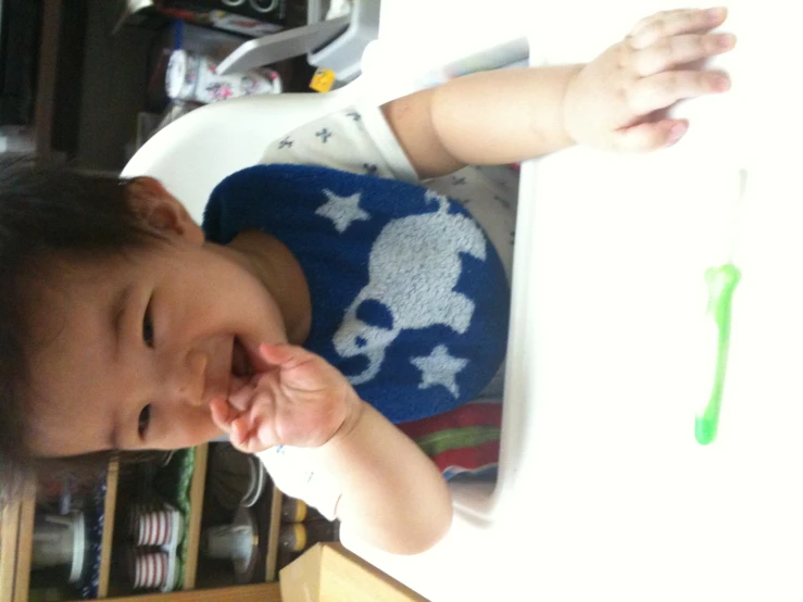 baby in high chair biting into plastic toothbrush