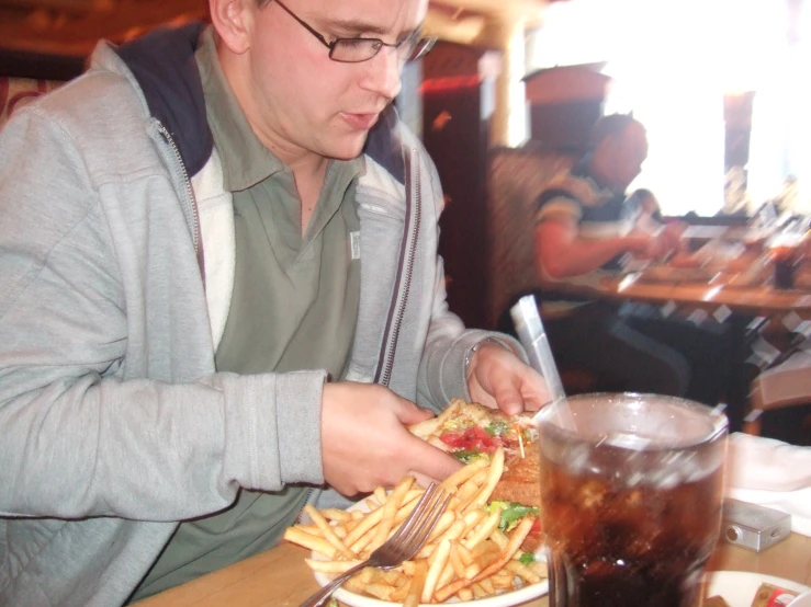 a man in glasses is eating french fries and looking at his food