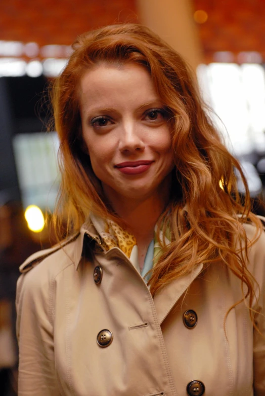 the smiling woman wearing a trench coat looks at the camera