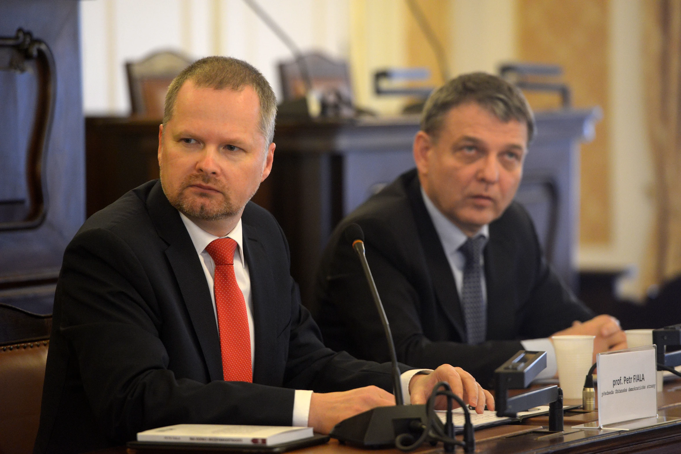 two men sit behind a table with laptops and other items