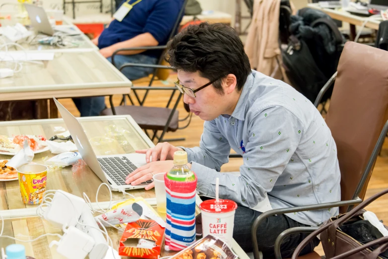 man in glasses and blue shirt at a table with a laptop and drink